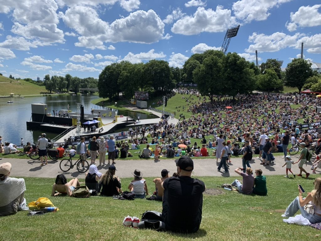 Publikum auf einer Wiese vor einer Open-Air-Bühne am See
